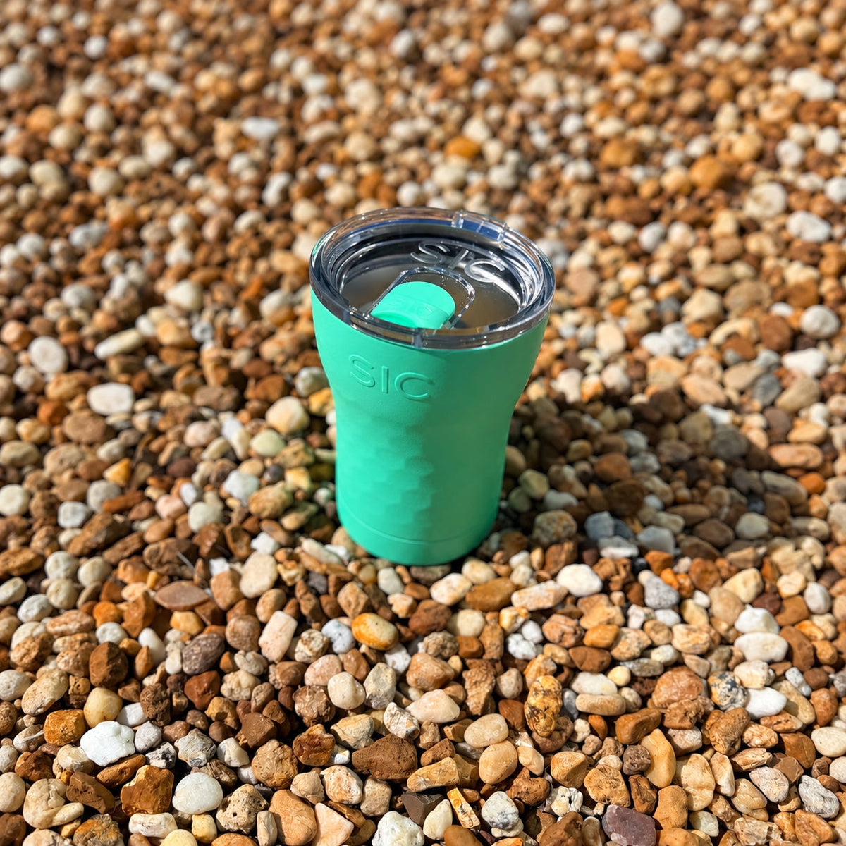 Overhead view of the clear lid on a SIC Hammered Mint 12 oz. tumbler on pebbles