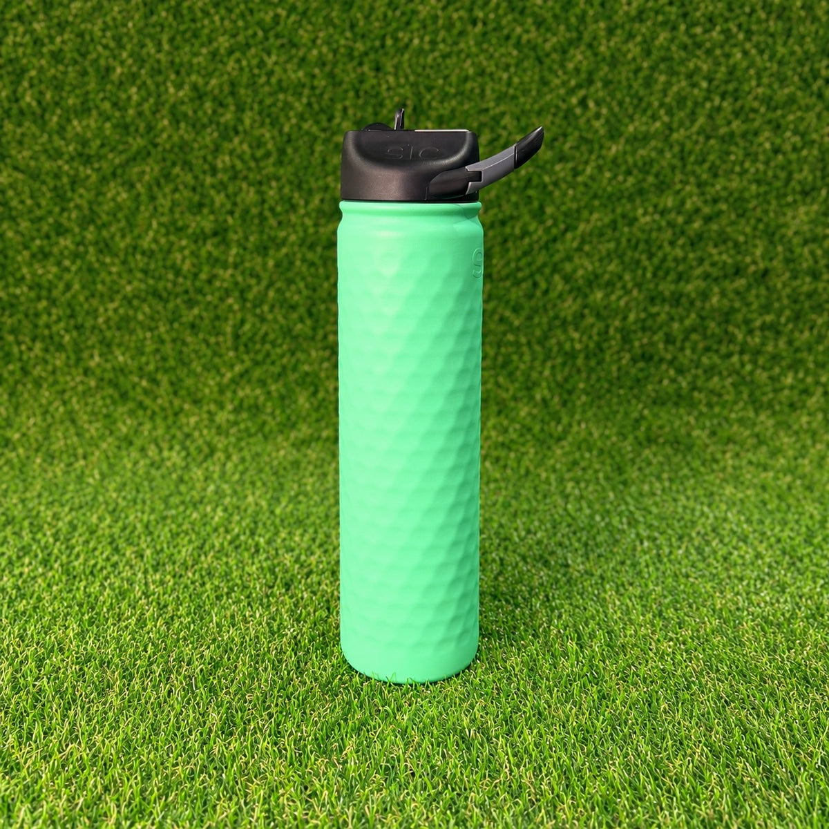 SIC Hammered Mint 27 oz. sport bottle with textured finish and black lid on green turf