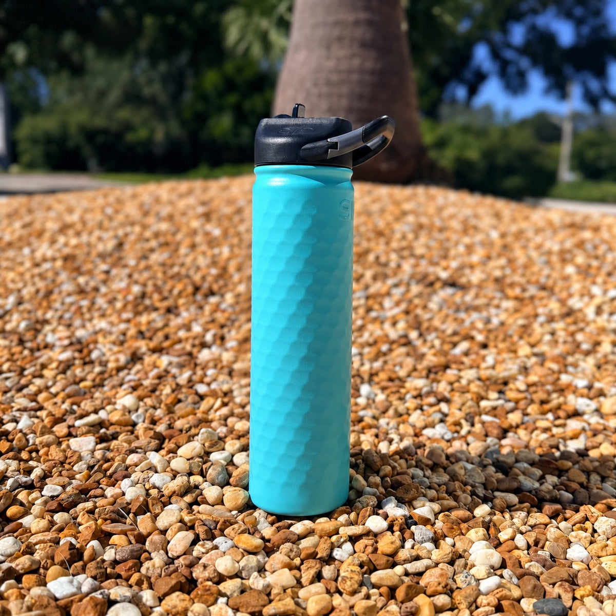 SIC Hammered Seafoam 27 oz. sport bottle with black carabiner lid on pebbles