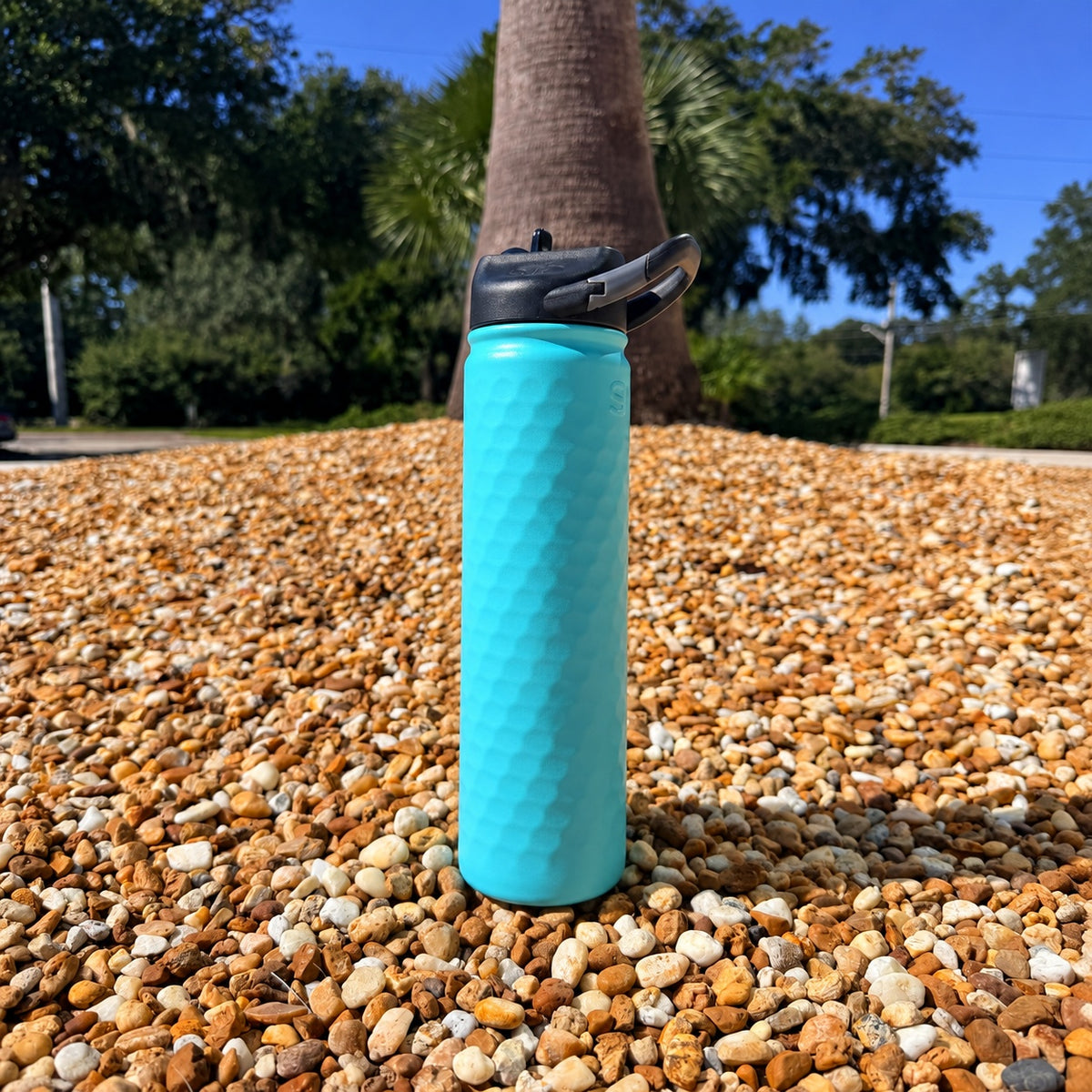 SIC Hammered Seafoam 27 oz. sport bottle with black carabiner lid on pebbles