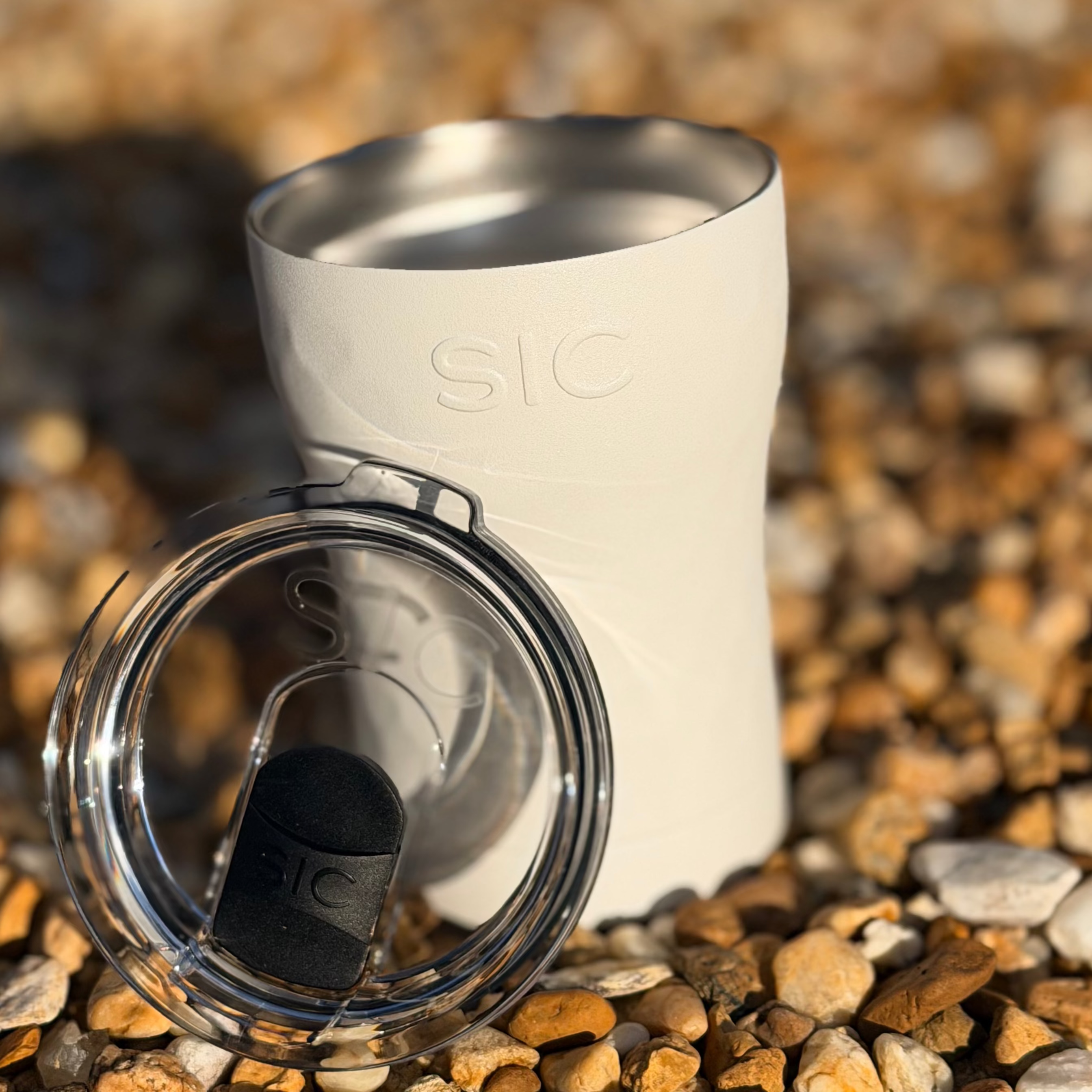 White tumbler with a clear lid on a pebbly surface
