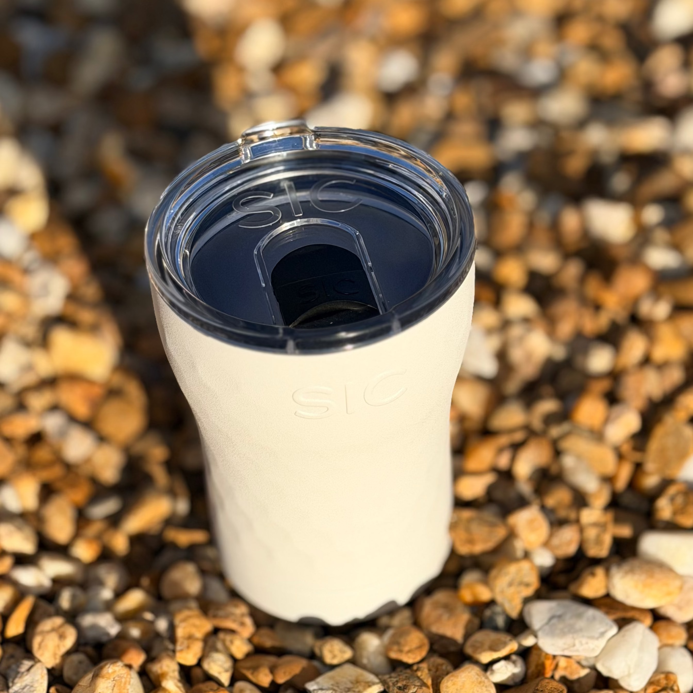 White tumbler with a blue lid on a bed of small stones