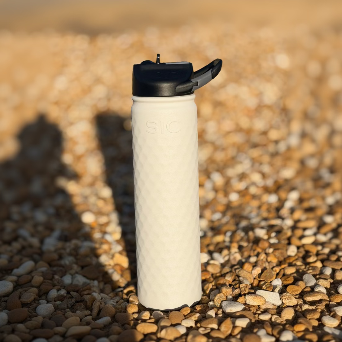White water bottle with black cap on a pebbly surface