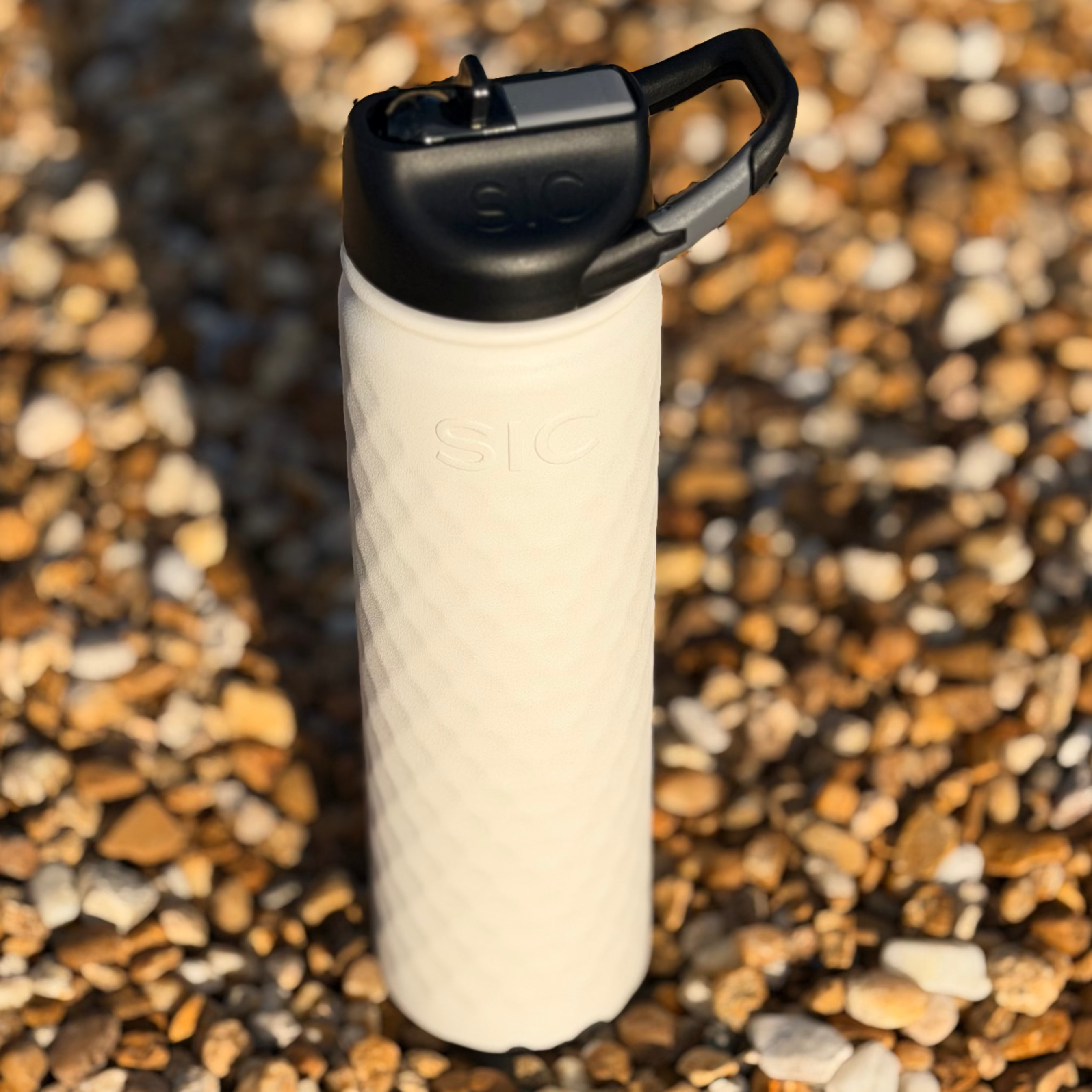 White textured water bottle with black lid on a pebbly surface