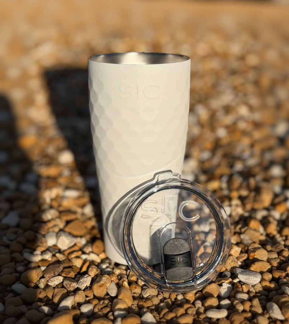 White tumbler with a clear lid on a gravel surface