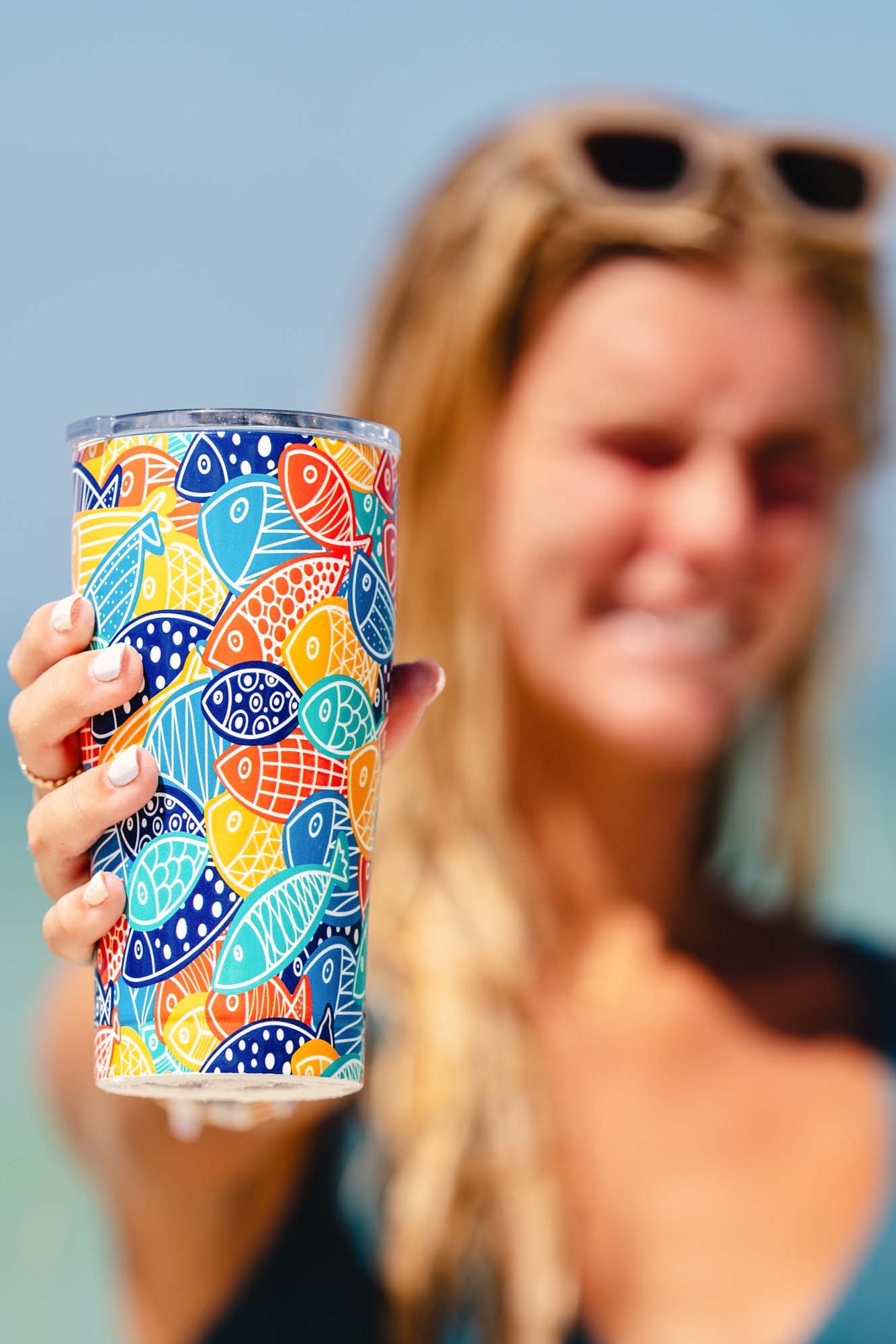 Woman holding a colorful patterned tumbler with a blurred beach background