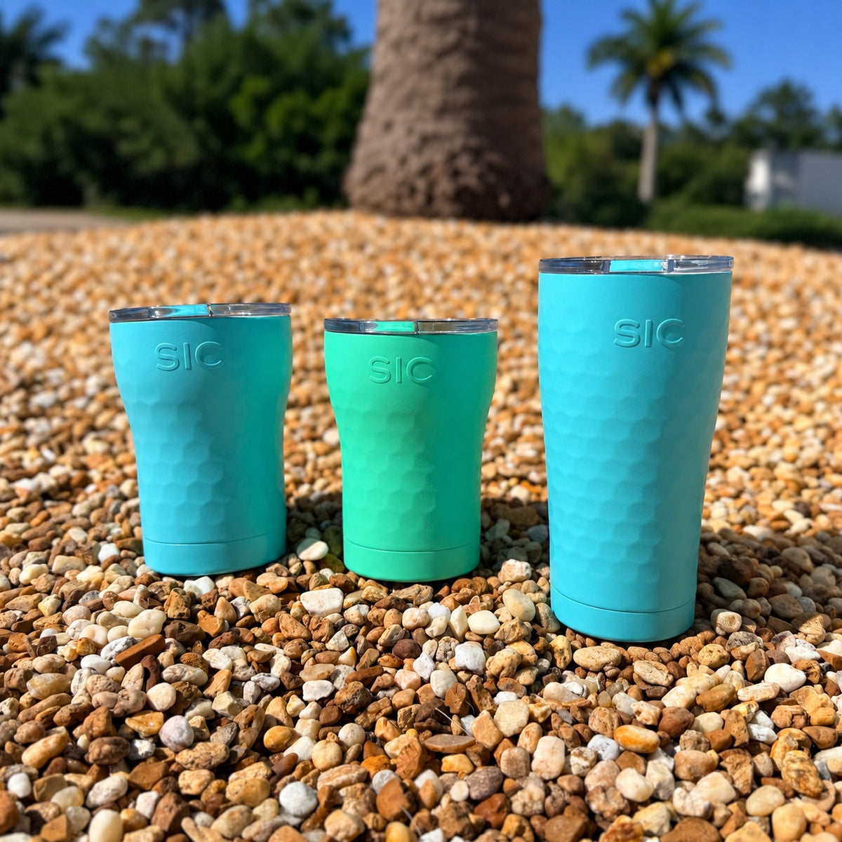 SIC Hammered Mint 12 oz. tumbler with Hammered Seafoam 12 oz. and 20 oz. tumblers on pebbles