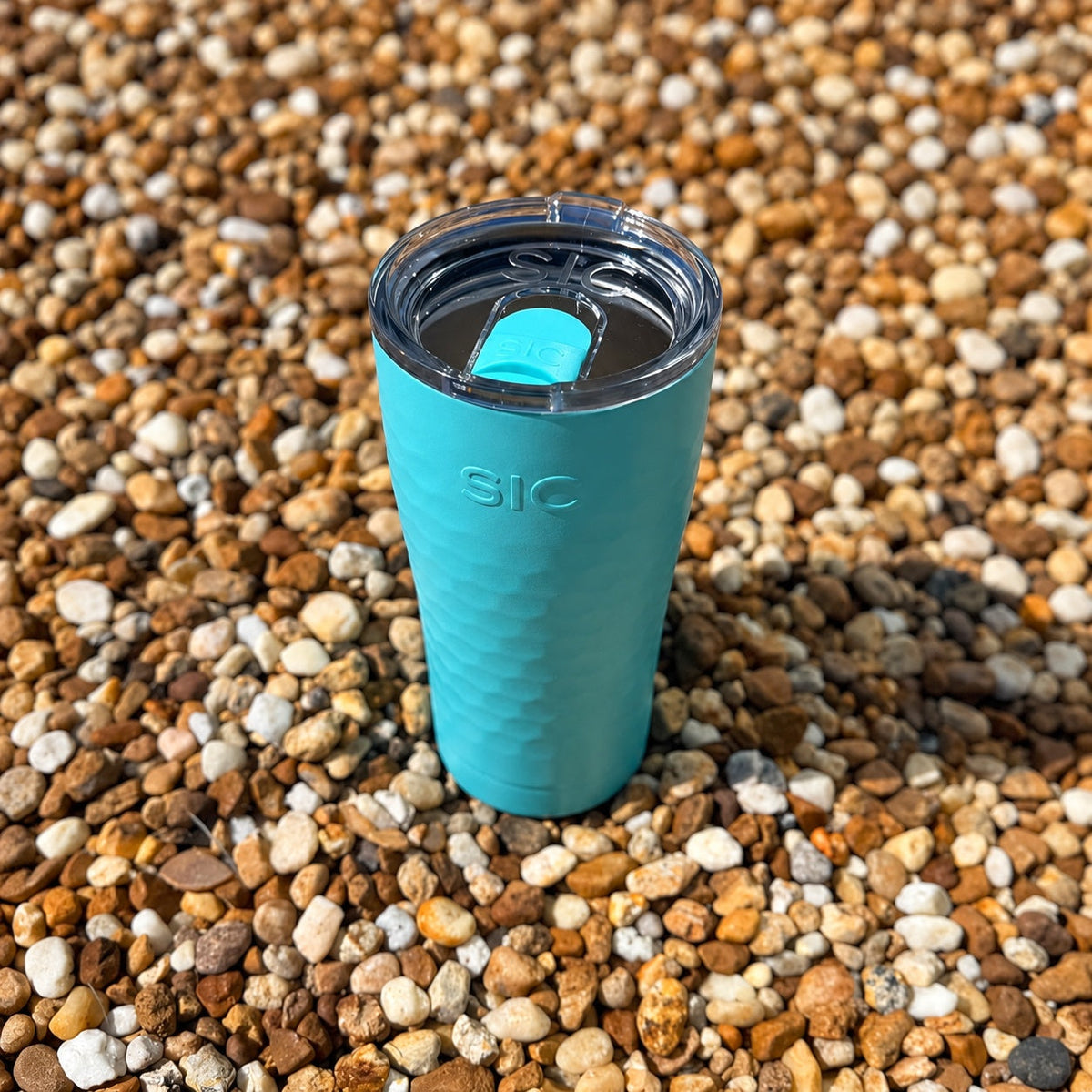 Overhead view of the clear lid on a SIC Hammered Seafoam 20 oz. tumbler on pebbles